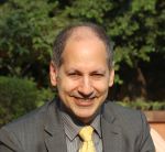 Head and shoulders of a white man in a grey suit and yellow tie