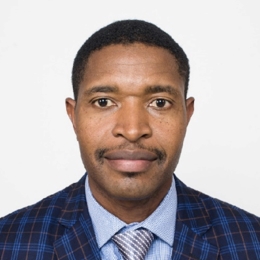 Black man with short black hair and blue suit smiling