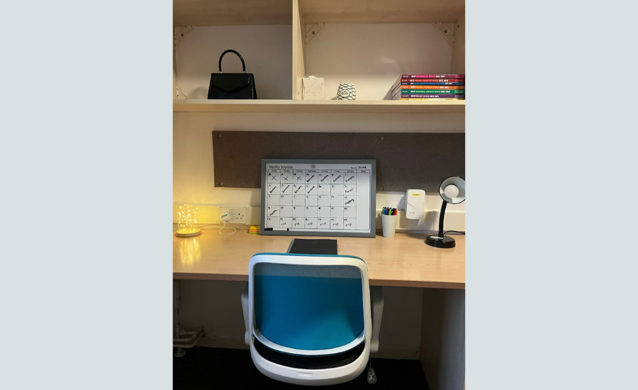 A corner of a desk, with a white board, stationary and books on desk &amp; cabinets.