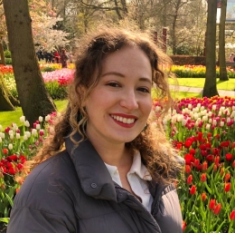 Woman with brown hair smiling in front of a garden with flowers