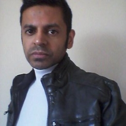 Man with short black hair wearing a white top and leather jacket