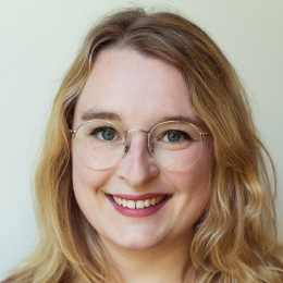 White woman with blonde shoulder length hair and glasses smiling
