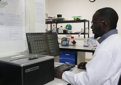 image of a man in a lab coat sitting in front of a computer with data on the screen