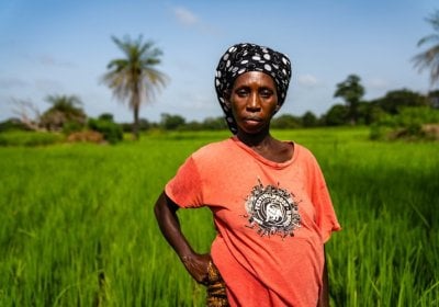 Black woman with orange t shirt standing in green field looking at the camera
