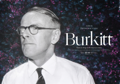 A black-and-white image of Dr Denis Burkitt against a background of an out-of-focus microscope slide