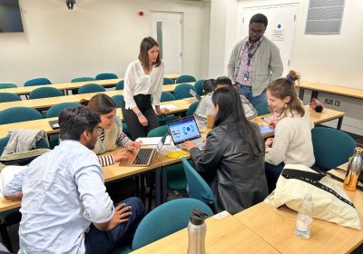 Group of students and staff working collaboratively on laptops around a table.