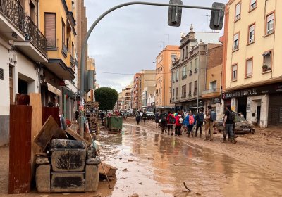 A commercial and residential street in Valencia is covered with muddy water. Muddy, broken furniture is piled on the side of the road.