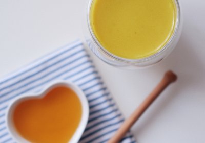 A glass containing turmeric golden milk, nearby a heart shaped dish containing honey