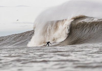 A photo of a surfer wearing a wetsuit riding a large, cresting wave